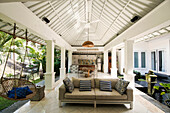 Offener Wohnbereich in einem tropischen Luxushaus mit Couch und Hängesessel
