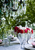 Gedeckter Tisch mit Gläsern und Blumenstrauß, darüber Kristall-Kronleuchter im Garten