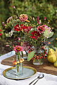 Bouquets of zinnias in glass containers with wreaths of berries