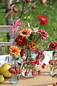 Bouquets of zinnias in glass containers with wreaths of berries
