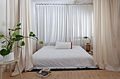 Minimalist bedroom with white bed, curtains and houseplant