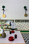 View over dining table to tiled wall with border and designer wall sconces