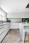 Modern kitchen with white units and herringbone parquet flooring