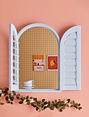 Arched window with light blue shutters on pink wall