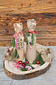 Christmas-wrapped bottles on wooden coasters with fir branches and baubles