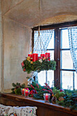 Hängender Adventskranz mit roten Kerzen, darunter weihnachtlich dekorierte Fensterbank