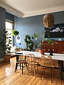 Tisch mit verschiedenen Stühlen und Grünpflanzen im Esszimmer mit blauen Wänden und Holzdielenboden