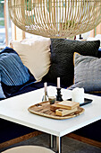 White coffee table with bamboo lamp above, pillow collection in the background