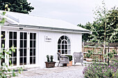 Holzhaus mit Sprossentüren und Rundbogenfenster, davor Sitzplatz