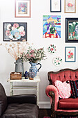 Antique sofa with cushions, broom table with flowers, above it pictures in rural living room