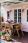 Holztisch mit klappbaren Rohrstühlen auf der Veranda eines rosa gestrichenen Hauses