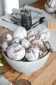 Marbled Easter eggs and feathers in a ceramic bowl on a wooden table