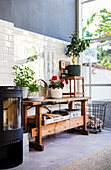 Wood-burning stove and wooden work bench against tiled wall in high-ceilinged conservatory