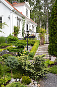 Gepflegter Vorgarten mit Steintreppe und vielfältigen Pflanzen vor weißem Haus