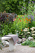 Stone bench with woollen blanket in flowering garden