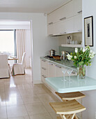 A modern open plan kitchen decorated in neutral colours breakfast bar area stools tiled floor view into dining room