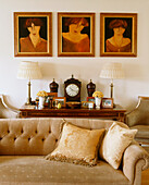 A detail of a traditional living room three framed paintings clock and ornaments on a wooden side table upholstered sofa