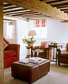 A traditional living room with exposed wooden beams above a leather coffee table in front of a red sofa