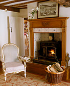 A country style living room traditional period armchair next to an open country fireplace and a wicker basket of logs
