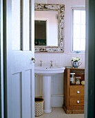 The view looking through the doorway into a traditional bathroom with an ornate framed mirror above a wash basin and next to a wooden cabinet