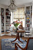 Library study with tulips on pedestal table below glass chandelier