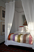 Four poster bed with mosquito netting and striped pastel blanket