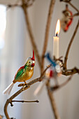 Weihnachtsschmuck in Form eines Papageis und einer Kerze auf einem Baumzweig
