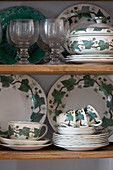 Collection of green and white tableware with leaf pattern displayed on wooden shelves