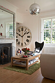 Wooden coffee table in front of fireplace next to oversize clock on wall