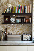 Open shelving and gold patterned wallpaper in kitchen of London fashion designer