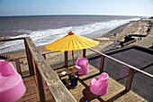 Rosa Sessel mit gelbem Sonnenschirm auf dem Balkon eines Strandhauses in Cromer in Norfolk, England, UK