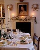Ein traditionelles Esszimmer dekoriert für Weihnachten Tisch für das Abendessen gedeckt Silber Kandelaber mit brennenden Kerzen Dekorationen auf dem Kaminsims Porträt Malerei