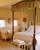A traditional yellow bedroom with pattern wallpaper four poster bed with canopy upholstered settee bedside cabinet stool