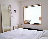 A modern bedroom with a large square window illuminating the bed with a large full length mirror opposite it