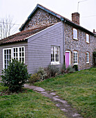Außenansicht eines Cottages aus Feuerstein mit einem Anbau aus Wetterschutzplatten