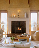 A traditional open brick fireplace in a sitting room with modern sofa armchairs coffee table and large windows