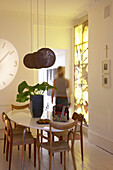 A modern dining room with black lampshades above a large oval dining table surrounded by traditional wooden chairs overlooked by a large wall clock projection
