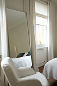 Detail of a modern bedroom full length mirror next to a window and behind a beige armchair