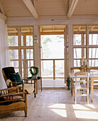 Country style sitting room with a wooden floor towards a veranda with windows and decking