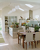 Eine moderne offene Wohnküche im Landhausstil mit Esstisch und Stühlen aus Holz, weißen Küchenschränken und einer offenen Tür nach draußen