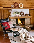A country living room with a stone fireplace lit fire timber ceiling leather chair