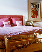 A traditional bedroom with double bed with upholstered headboard in red check fabric old fashioned wooden cot