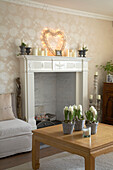 Detail of traditional country style sitting room fireplace with heart shaped illumination on it and low wooden table with flowers in baskets in front of it