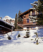 Außenansicht eines traditionellen Schweizer Holzchalets mit Schnee, Tannen und Bergen