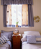 A detail of a country style bedroom two single beds blue curtains with matching bed linen wicker bedside cabinet tray with coffee pot