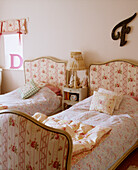 Traditionelles Gästeschlafzimmer mit zwei Einzelbetten mit gepolsterten Kopf- und Fußteilen und Nachttischlampen mit Blumenmuster