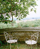 Schmiedeeiserne Stühle vor Mauer mit Blick auf eine ländliche Landschaft