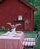Ein außerhalb Detail eines Tisches für das Mittagessen in einem Garten Stühle mit rosa gestreiften Kissen Holzhaus im Hintergrund