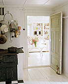 A country kitchen in neutral colours sitting room seen through an open door painted floorboards door stop utensils and pans hanging from wall