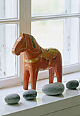 A detail of a carved painted wooden horse a collection of stones placed on a window sill